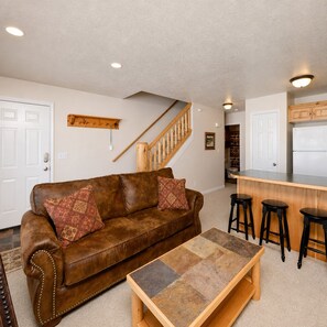 A living room with a brown leather sofa, a coffee table, and a kitchen area with stools. - Ski Condo and Summer Resort (Eden)