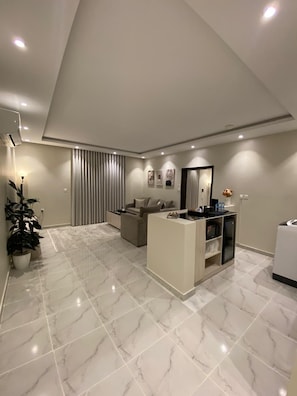 Un soggiorno moderno con soffitto alto, un divano, un tavolino da caffè e un piccolo armadietto bianco.