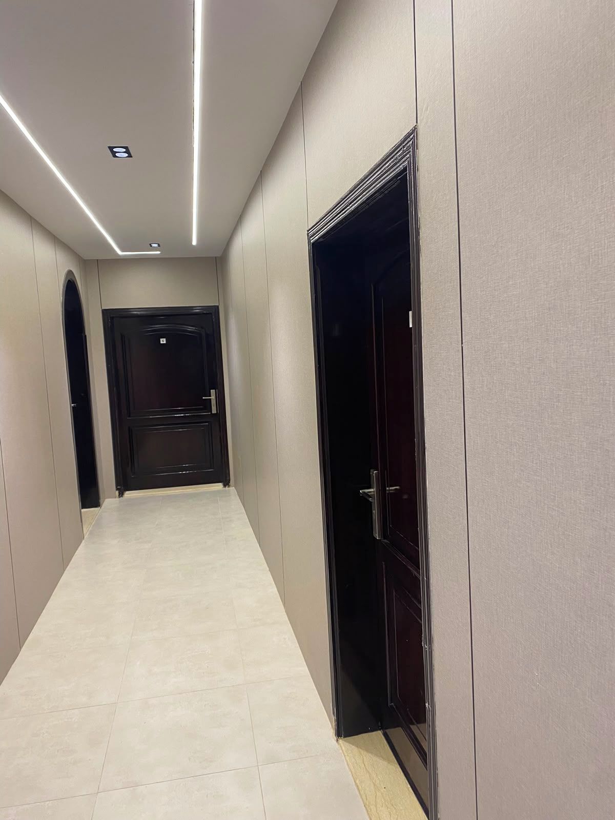 A hallway with a tiled floor, a door on the right, and a door at the end.