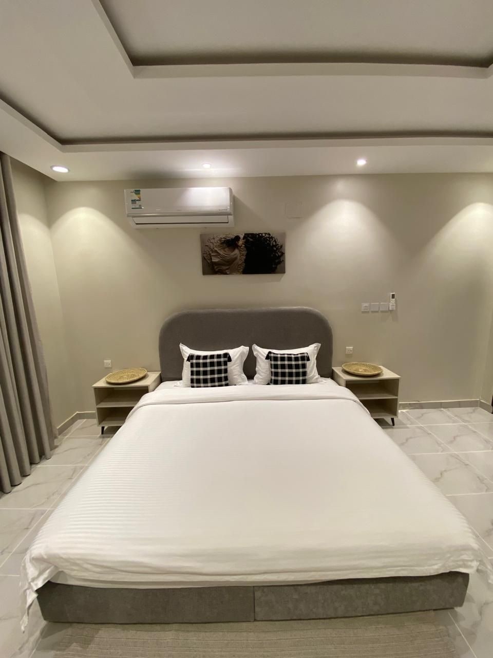 A modern bedroom with a large bed, bedside tables, and a wall-mounted air conditioner.