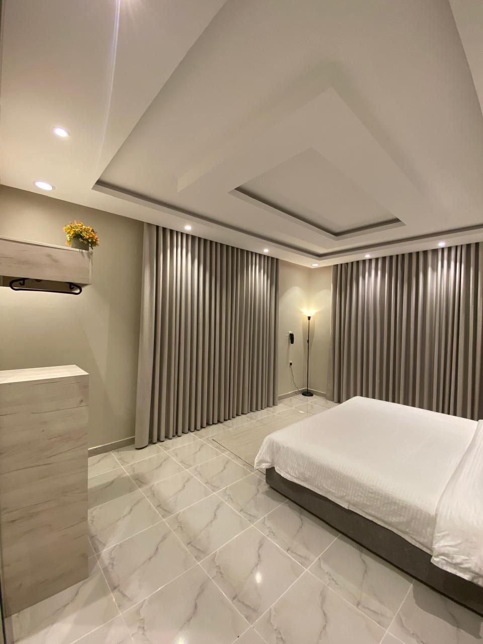A modern hotel room with a large bed, a built-in wardrobe, and a floor lamp.