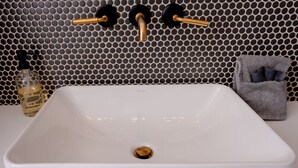 Ein weißes, rechteckiges Waschbecken mit einem Abfluss, einer Seifenflasche und einem Handtuch auf einer weißen Arbeitsplatte.