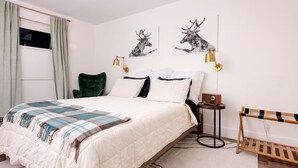 Ein Schlafzimmer mit einem Bett, einem grünen Sessel, einem Nachttisch mit Lampe und einer Holzbank.