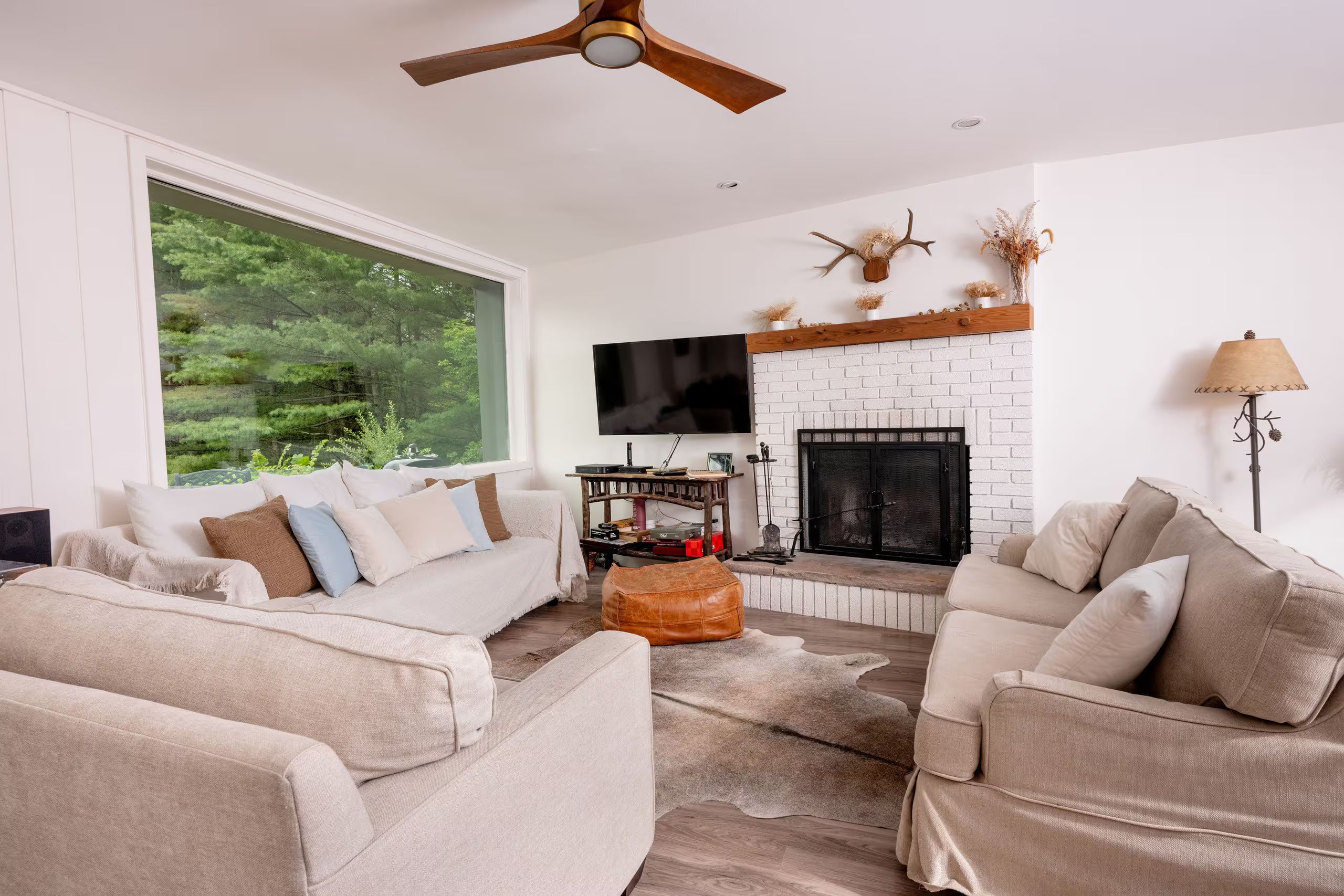 A modern living room with a fireplace, a large window, and a ceiling fan.