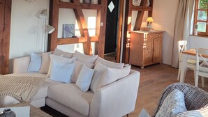 Un accogliente soggiorno con un divano bianco, una poltrona in vimini, un soffitto in legno e una sveglia appesa al muro.