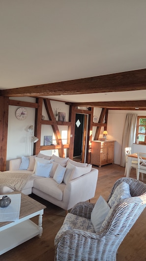 A cozy living room with a white sofa, a wicker chair, a wooden ceiling, and a clock on the wall. - Vrbo Property (Scheibenhard)