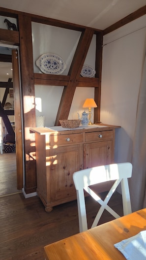 A wooden cabinet with drawers, a white chair, and a table with a lamp. - Vrbo Property (Scheibenhard)