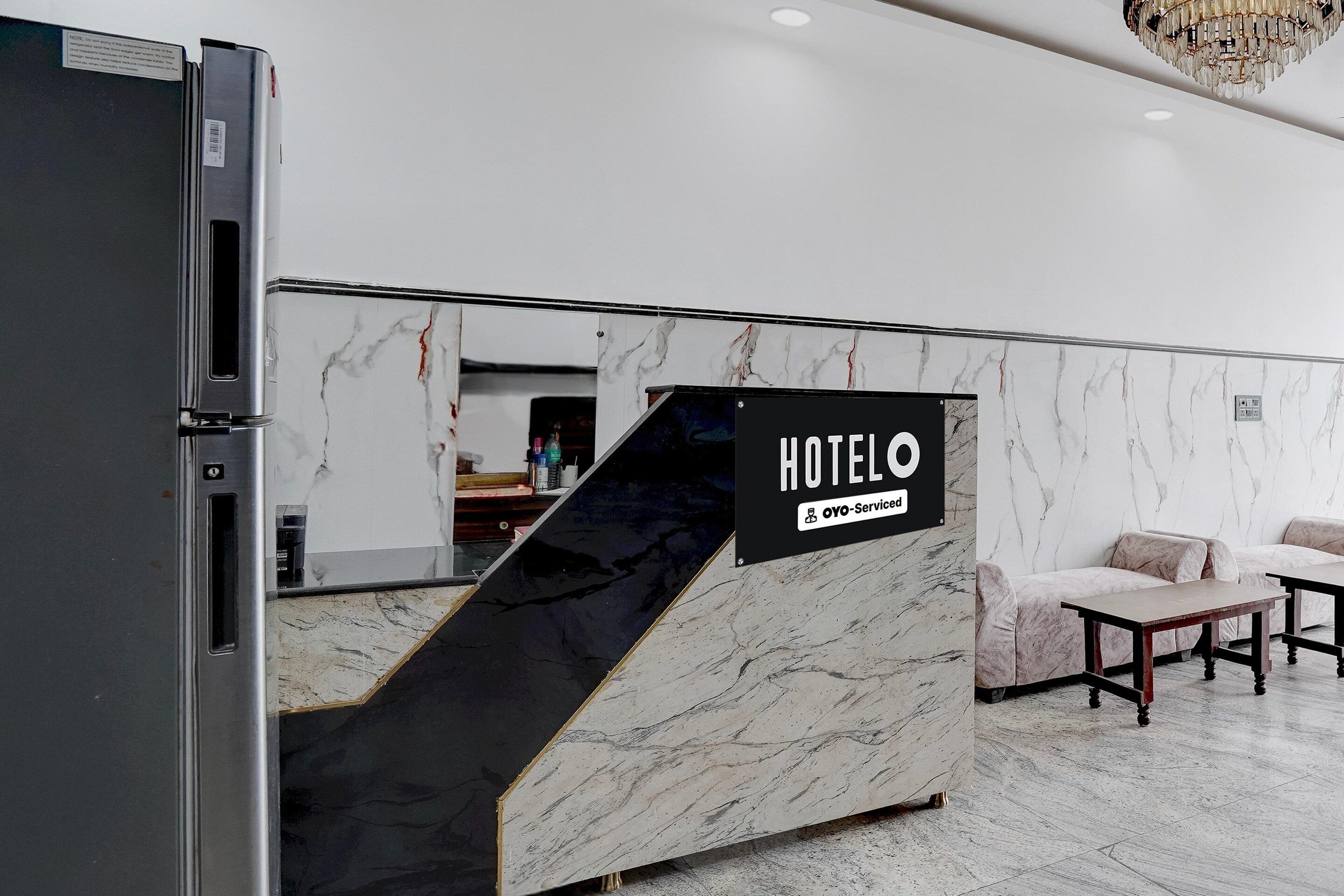 Taulell de recepció d'hotel amb una paret de marbre, un cartell que diu 'HOTELO OYO-Service' i una làmpada de cristall moderna.