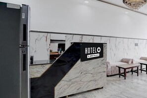 A hotel reception desk with a marble wall, a sign reading 'HOTELO OYO-Service', and a modern chandelier. - Super Deluxe Room Xponest Hotel (Greater Noida)
