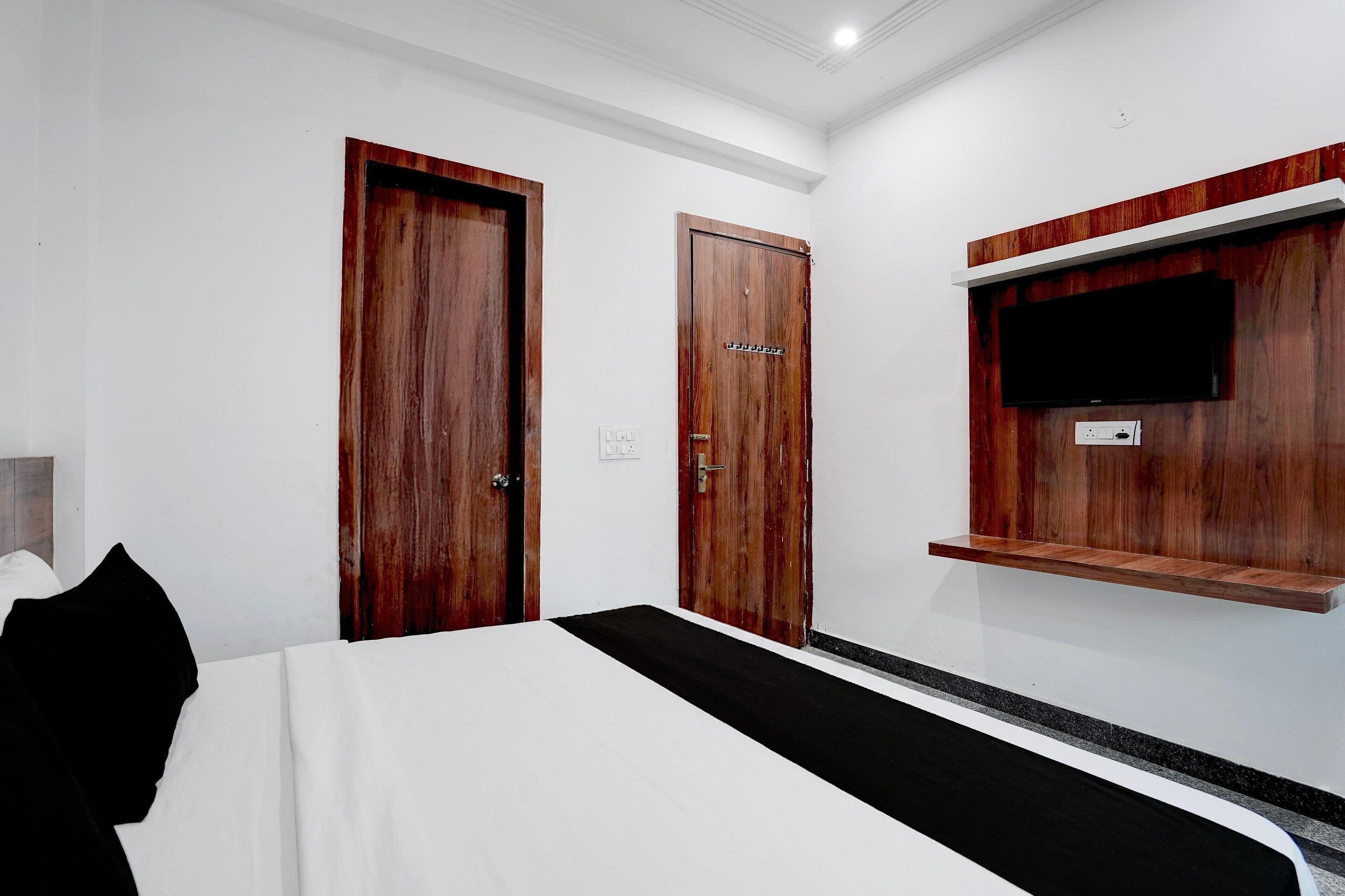 Habitación de hotel con una cama, dos puertas de madera, un televisor montado y un pequeño estante.