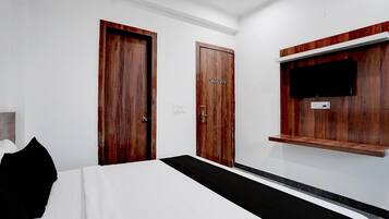 Habitación de hotel con una cama, dos puertas de madera, un televisor montado y un pequeño estante.