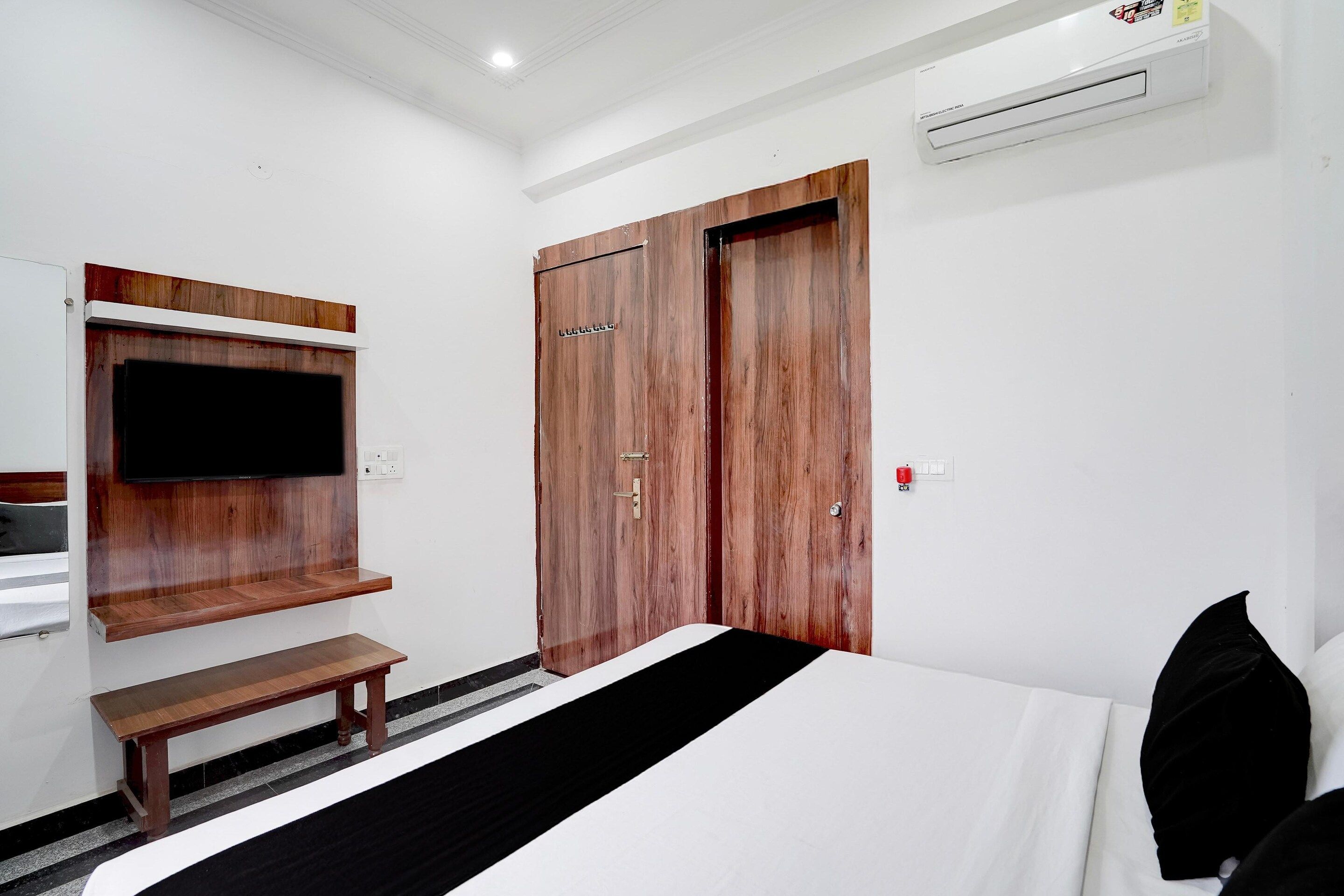 Una habitación de hotel con una cama, un banco, un televisor montado en la pared y un armario.