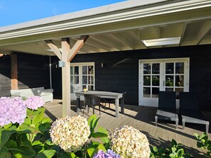 Eine überdachte Terrasse im Freien mit Tisch und Stühlen, umgeben von Hortensien.