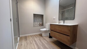 Un baño con inodoro, lavamanos, espejo y una pequeña ventana con estampado floral.