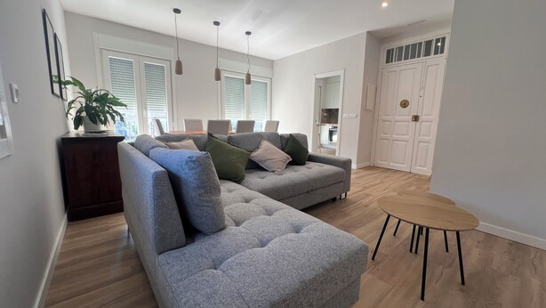 Una sala moderna con un sofá seccional gris, una mesita de madera y una planta en maceta.