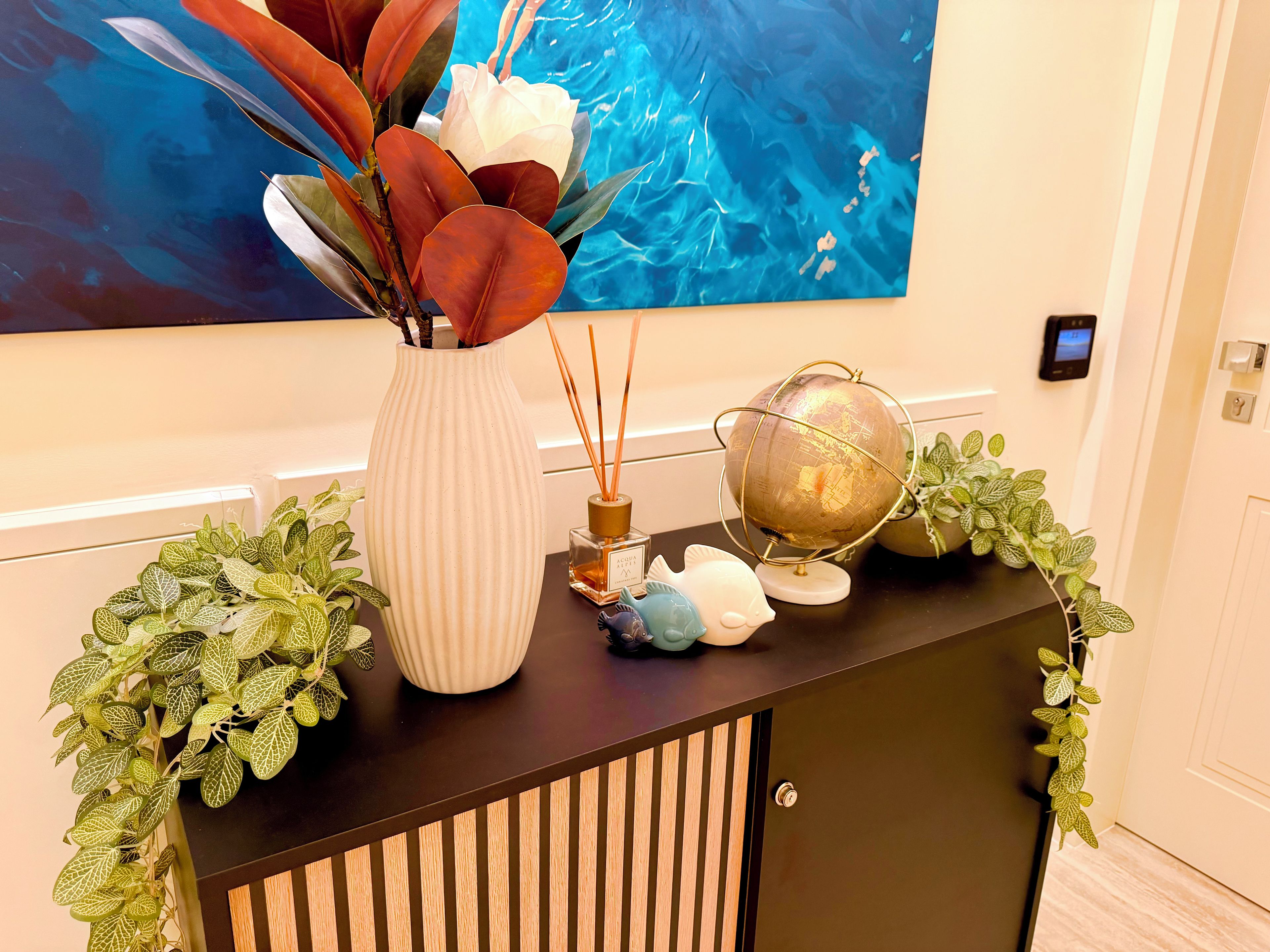 Une console décorative ornée d’un vase de fleurs, d’un globe terrestre et d’une petite statuette.
