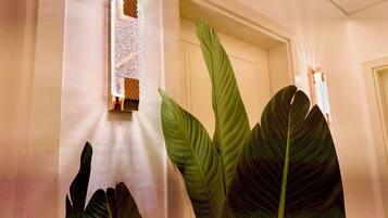 A hallway with a door, a wall-mounted light fixture, and large green leaves.