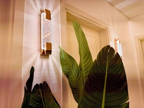 Un couloir avec une porte, un luminaire fixé au mur et de grandes feuilles vertes.