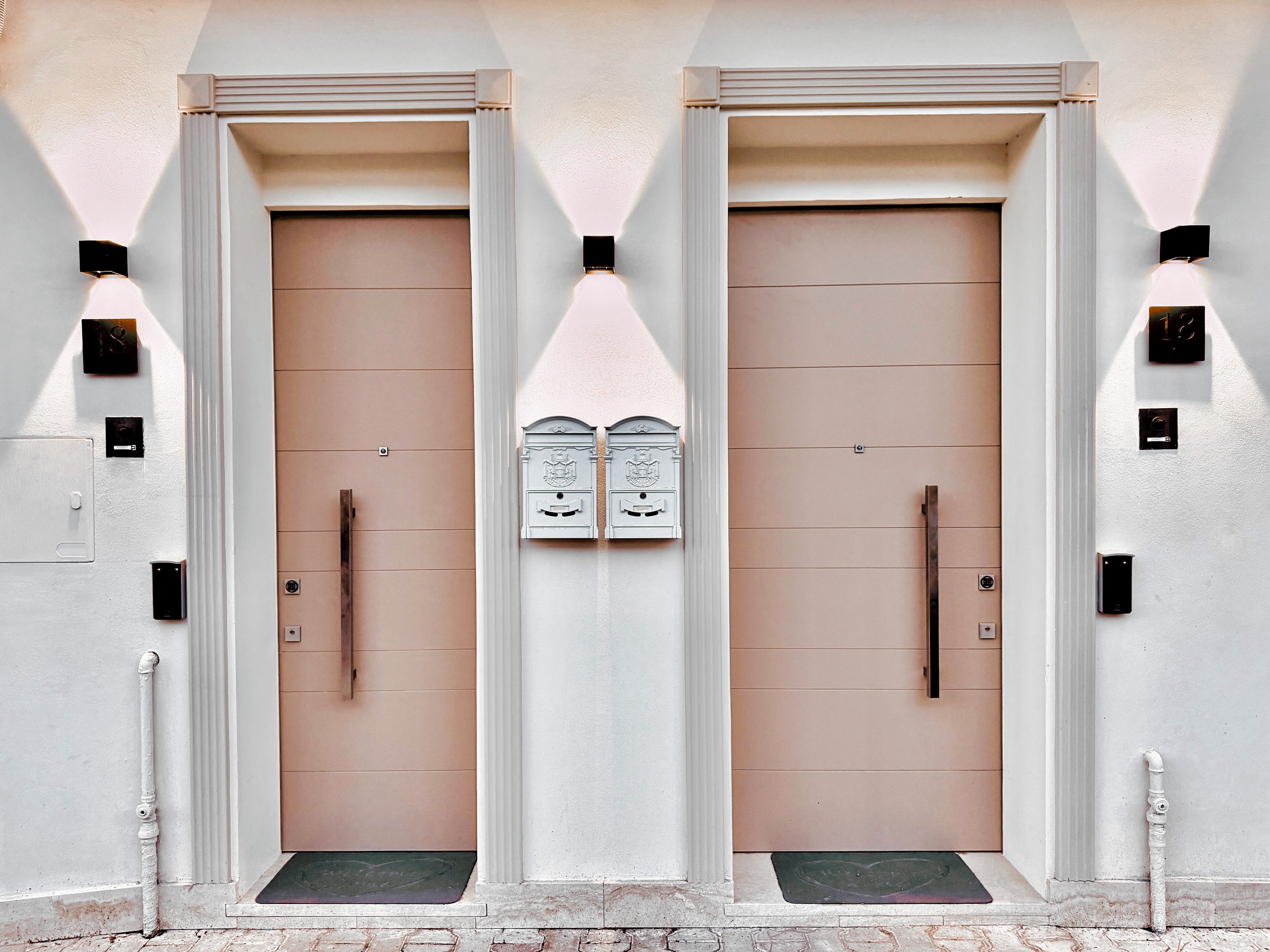 Une façade d’immeuble avec deux portes symétriques, chacune dotée d’une poignée et d’une petite fenêtre au-dessus.
