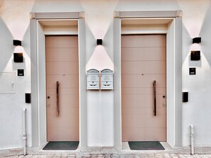 Une façade d’immeuble avec deux portes symétriques, chacune dotée d’une poignée et d’une petite fenêtre au-dessus.