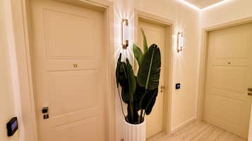 Corredor com três portas fechadas, um vaso de planta e um luminário fixado na parede.