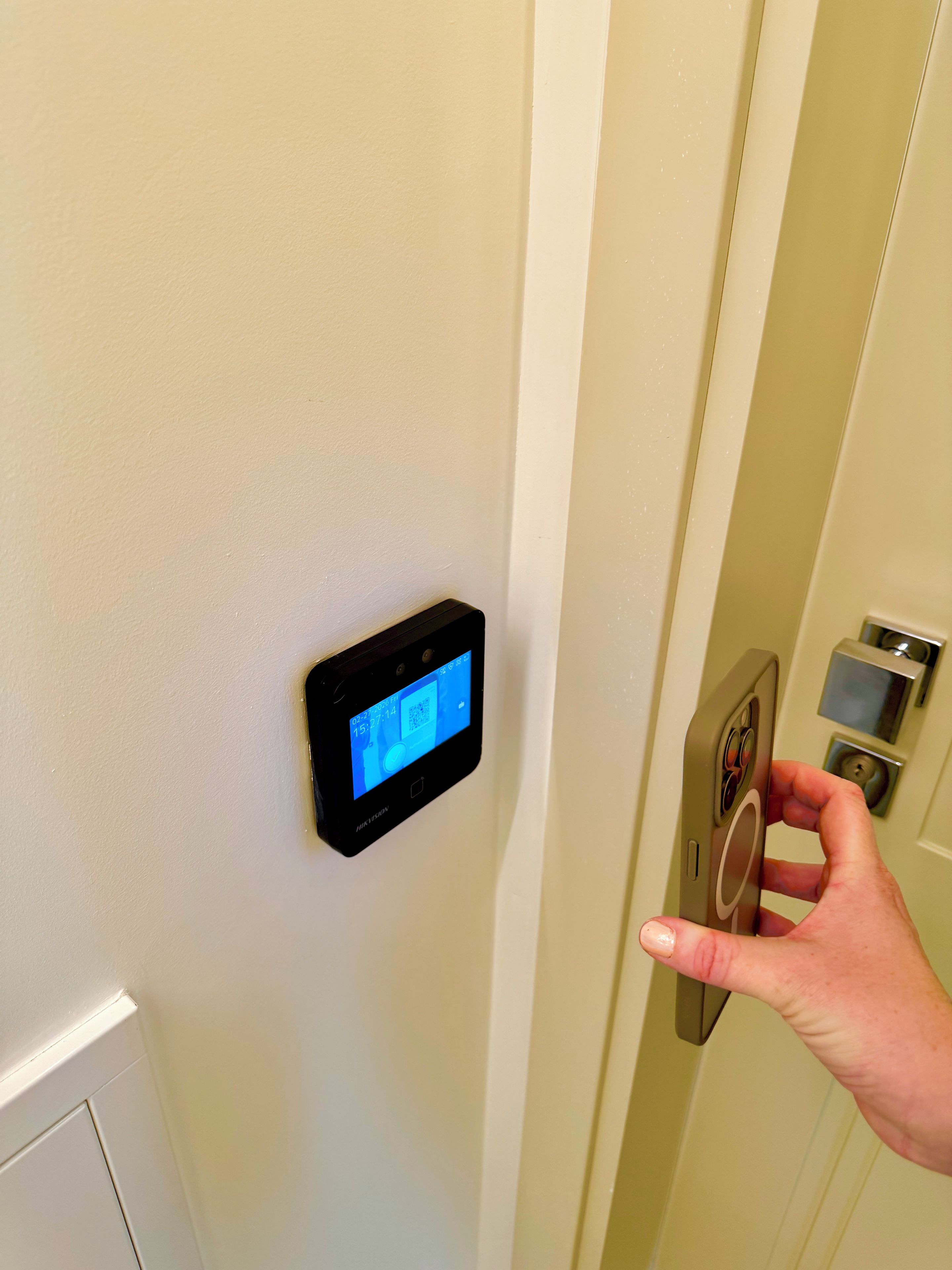 Una mano operando una cerradura digital en una puerta, con un panel de control que muestra la hora y la temperatura.