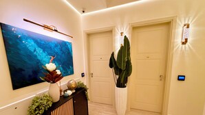Un corridoio con un grande quadro astratto, un tavolo consolle con oggetti decorativi, due porte e luci a parete.