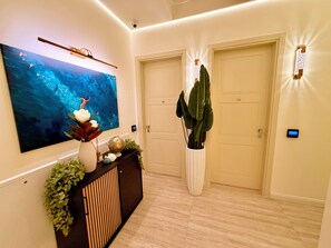 Un couloir orné d’un grand tableau abstrait, d’une console sur laquelle sont disposés des objets décoratifs, de deux portes et de luminaires fixés au mur.