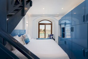 A bedroom with a bed, a view through a window, and blue cabinets. - Vesta Luxury Apartment -1br - New Nubia (El Gouna)