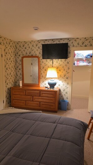 Ein Schlafzimmer mit Bett, Kommode, Spiegel, Lampe und Fernseher an der Wand.