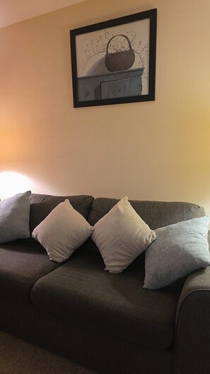 A dark-colored sofa with three pillows and a framed picture above it. - Perfect 2-bedroom house in amazing Lake Harmony getaway (Lake Harmony)