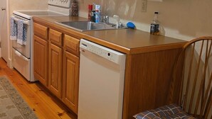 A kitchen with wooden cabinets, a microwave, a stove, a dishwasher, and a chair with a cushion. - Perfect 2-bedroom house in amazing Lake Harmony getaway (Lake Harmony)