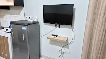 Una cocina compacta con un refrigerador, un televisor de pantalla plana montado en la pared y un pequeño estante de madera.
