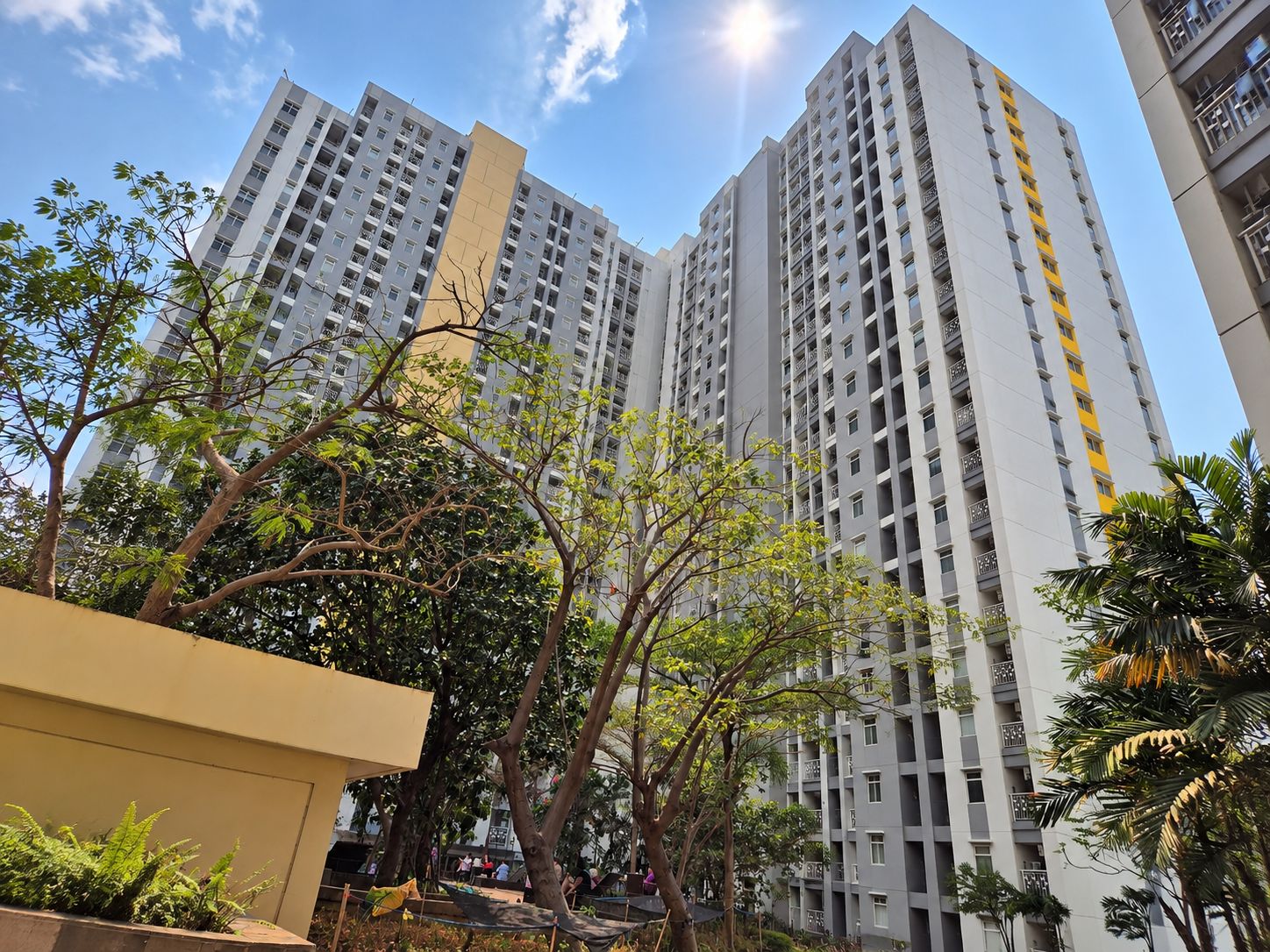 A high-rise residential building with multiple balconies, surrounded by trees and greenery.