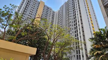 A high-rise residential building with multiple balconies, surrounded by trees and greenery.