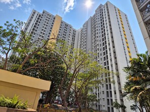 Un edificio residencial alto con varios balcones, rodeado de árboles y vegetación.