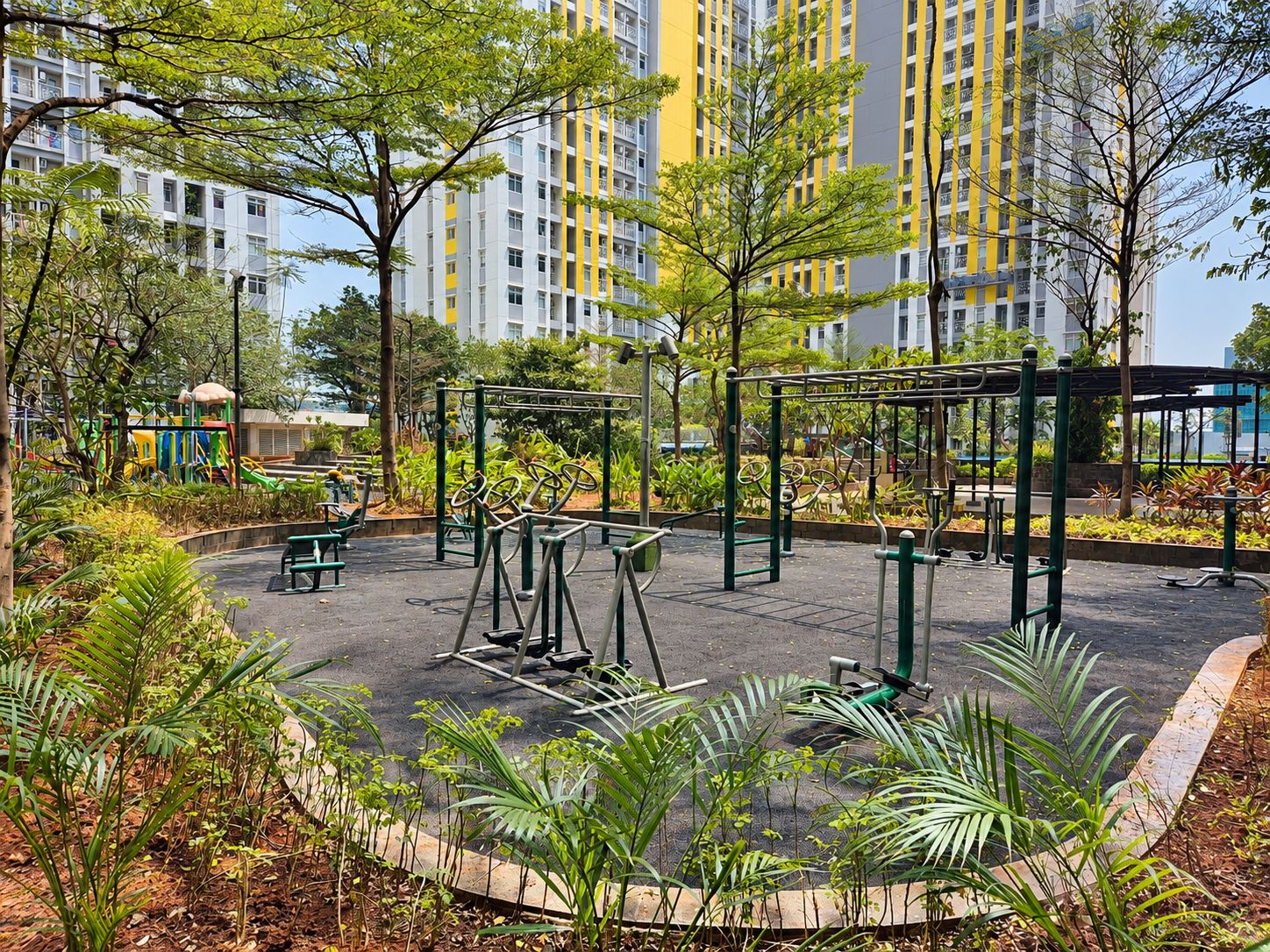 A playground with exercise equipment surrounded by greenery and a residential building in the background.