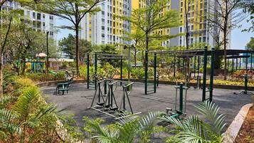 A playground with exercise equipment surrounded by greenery and a residential building in the background.