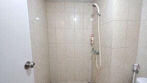 A small, tiled shower room with a handheld showerhead, a bottle of shampoo, and a toilet. - Nusantara Rooms Springlake By Reccoma (Bekasi)