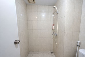 Ein kleines Duschbad mit gefliesten Wänden, einer Handbrause, einer Shampooflasche und einer Toilette.