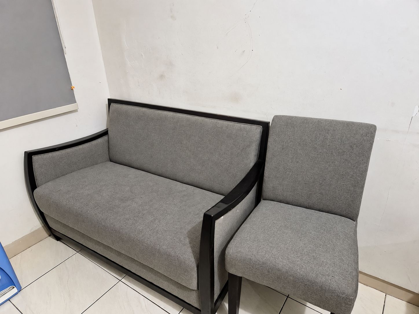 A grey sofa and chair with black frames, positioned against a plain wall with a visible crack.