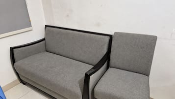 Un sofá y un sillón grises con estructura negra, ubicados frente a una pared lisa que presenta una grieta visible.