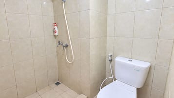 Un baño con inodoro, ducha con cabezal de ducha manual y dispensador de jabón en la pared.