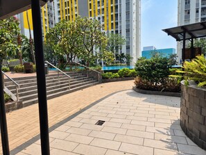 A courtyard with a staircase leading to a building, surrounded by greenery and a pool. - Nusantara Rooms Springlake By Reccoma (Bekasi)