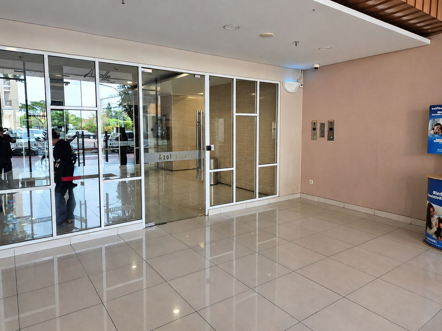 Un vestíbulo moderno con puertas de cristal, piso de baldosas y un ascensor empotrado en la pared.