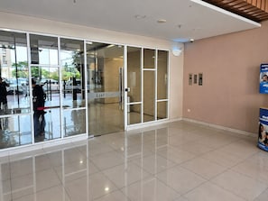 A modern lobby with glass doors, a tiled floor, and a wall-mounted elevator. - Nusantara Rooms Springlake By Reccoma (Bekasi)