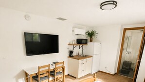 Ein Schlafzimmer mit Bett, Schreibtisch, Stuhl, Fernseher, Mikrowelle und Dusche.