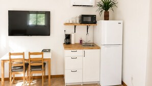 Een compact woongedeelte met een kitchenette, een eethoek met twee stoelen, een flatscreen televisie aan de muur en een potplant.