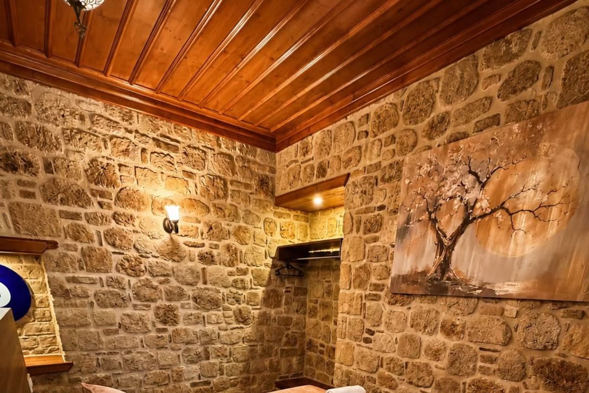 A bedroom with a stone wall, wooden ceiling, a bed with pillows, a towel rack, and a painting.