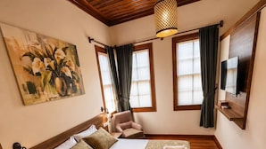 A bedroom with a wooden ceiling, a bed with a green bedspread, a painting on the wall, and a TV mounted on the wall. - Sais Hotel Kaleiçi (Antalya)